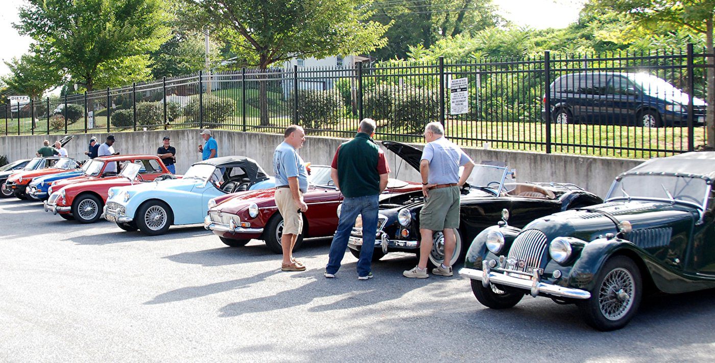 A group of men standing next to classic cars.