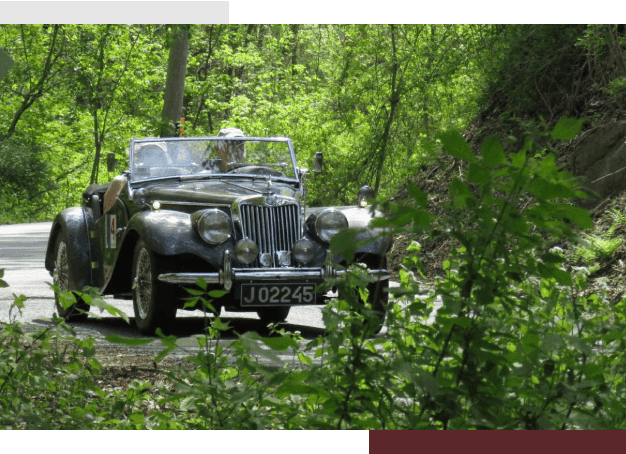 A vintage car driving down the road in the woods.
