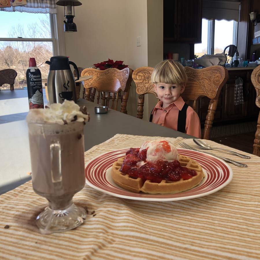 A young boy looks on as his waffle and ice cream are served.