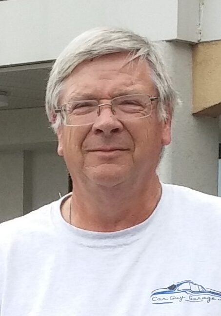 A man with glasses and white hair wearing a t-shirt.
