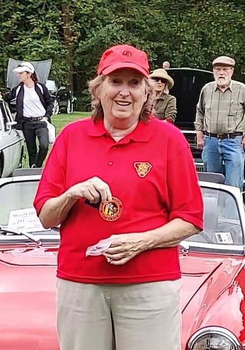 A woman in red shirt holding something near some cars.
