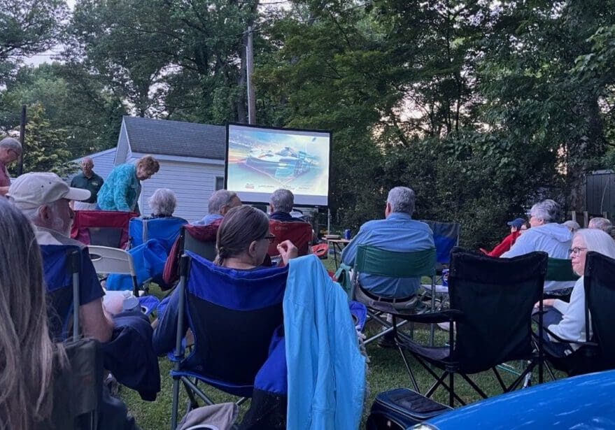 Outdoor movie screening with people seated in folding chairs.